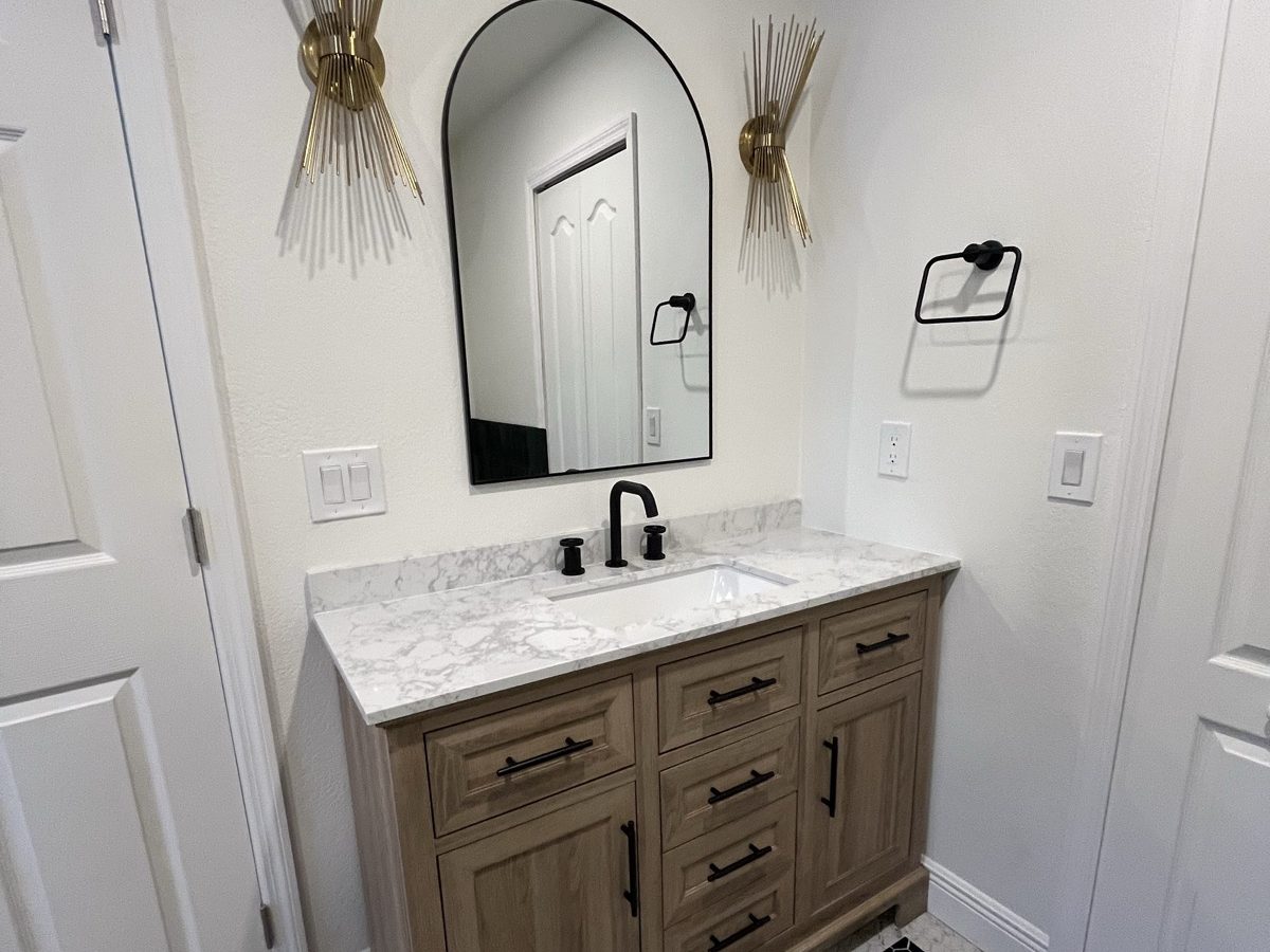 Powder bath with an arched mirror, wood vanity and designer sconces