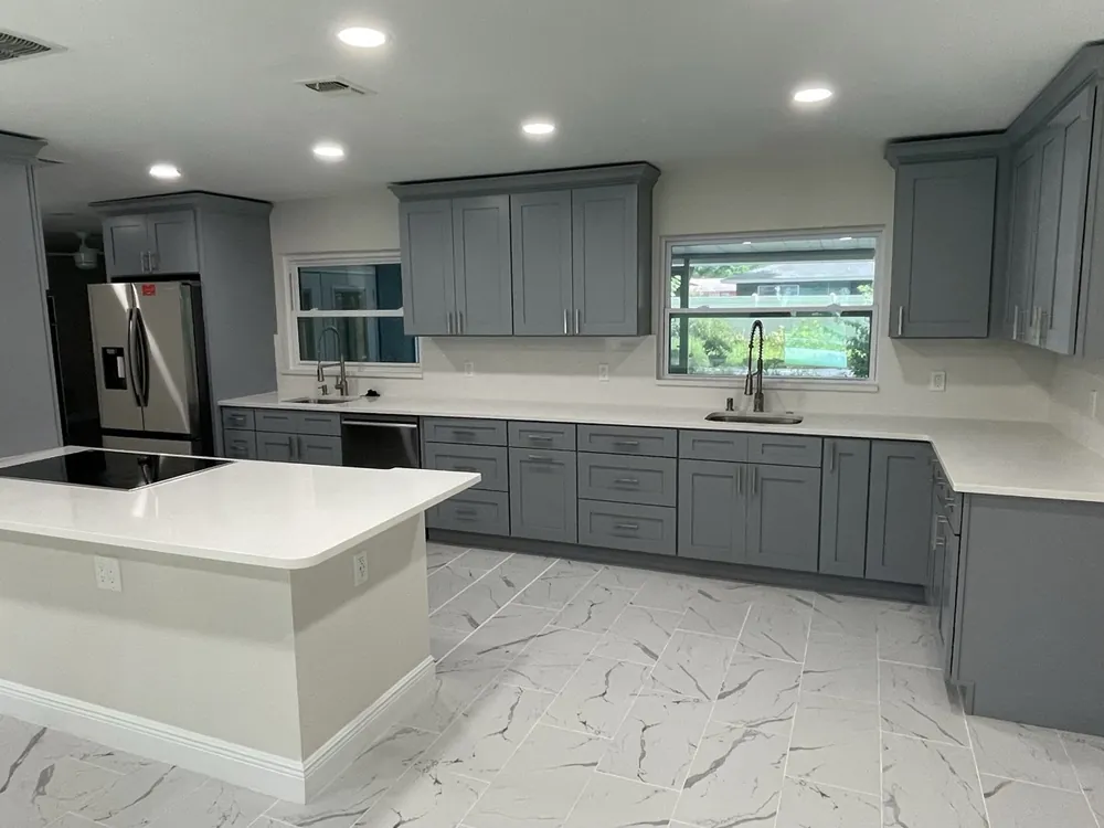 Kitchen with gray cabinetry, a quartz waterfall island and marble-look tile floor